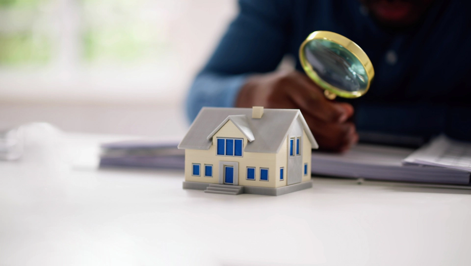 man holding magnifying glass and miniature house